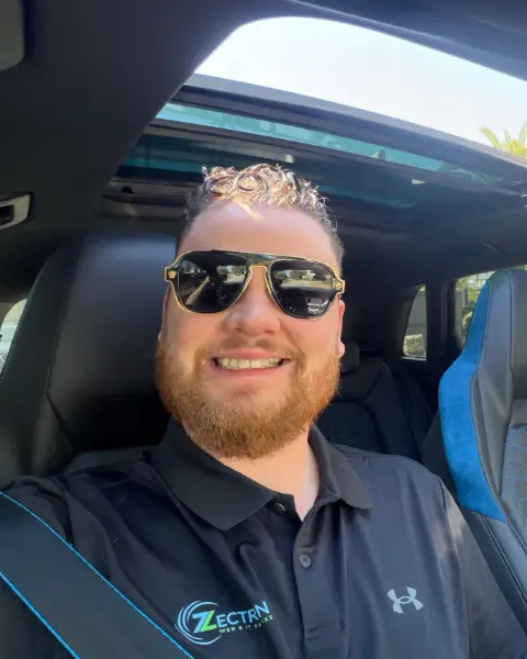 Zac Tassone, Zac the IT Guy, smiling in his car in a Zectron polo